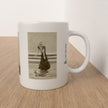 A white ceramic mug with a sepia-toned vintage illustration of a woman in a dress, sitting on a light wood tabletop against a white wall.