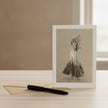 A greetings card showing ginger rogersstanding on a light wood surface next to a kraft envelope and a black pen.