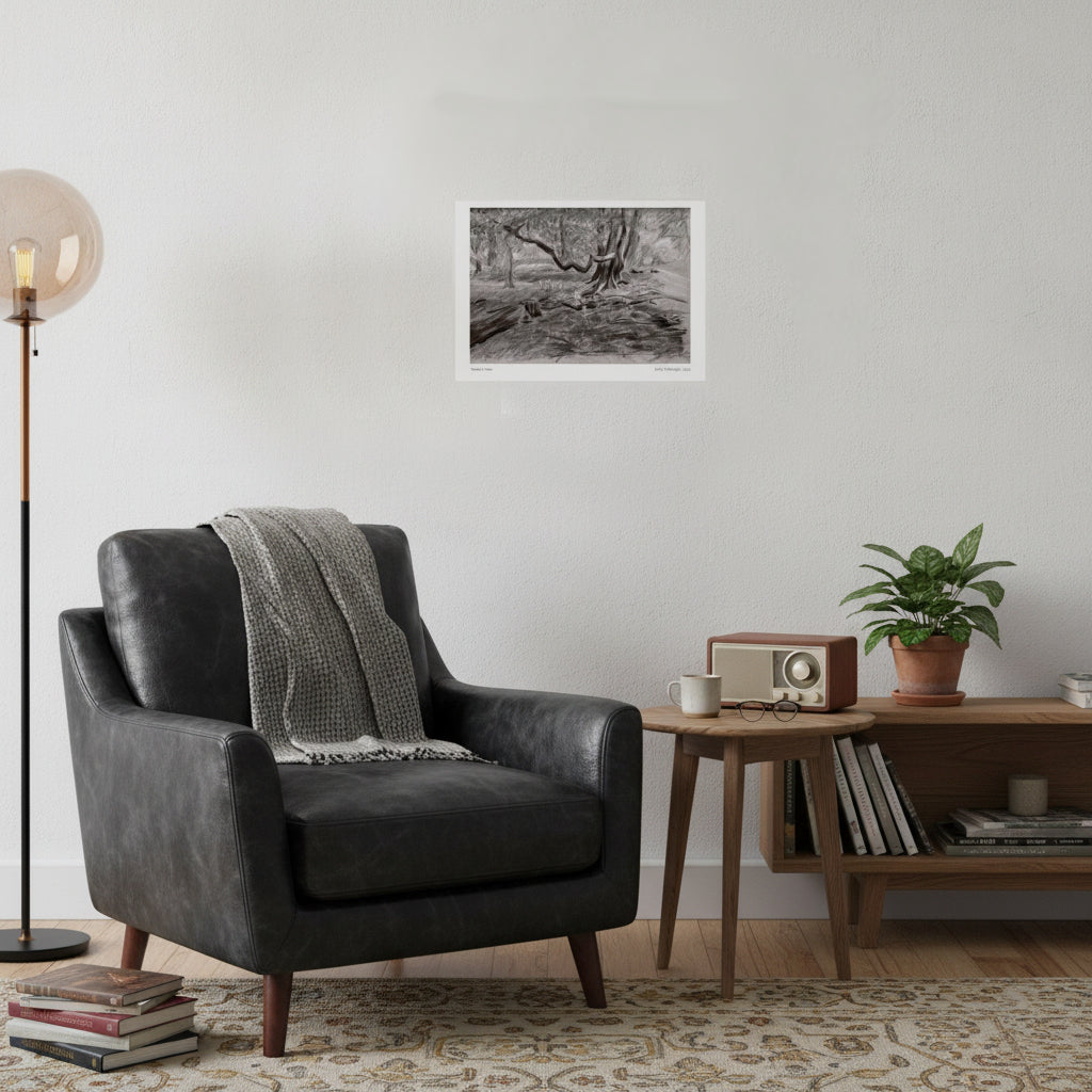 A black and white landscape art print of a tree is displayed on a white wall in a styled living room setting with a dark gray leather armchair, a wooden side table, a potted plant, and a floor lamp.