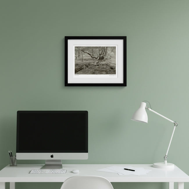 A framed black and white landscape art print hangs on a light gray wall above a dark wood sideboard with silver goblets, a glass decanter, and a bowl of fruit.