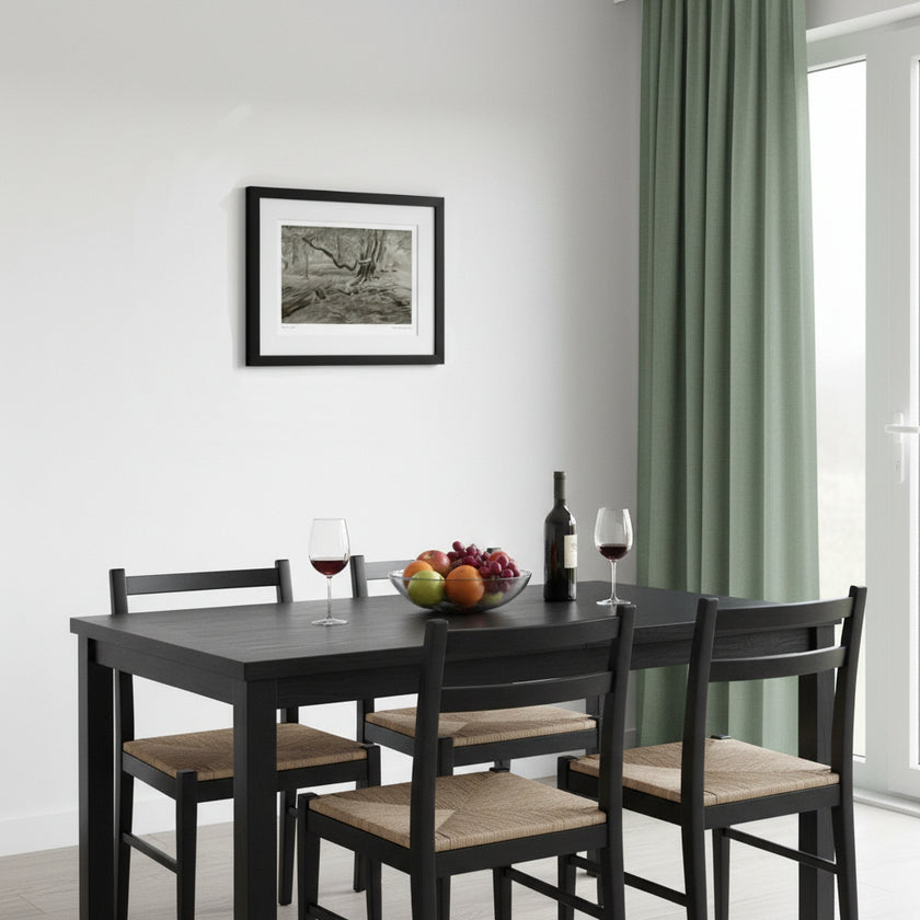 A black wooden dining table with four matching chairs featuring natural woven seats, styled with a wine bottle, two glasses of red wine, and a fruit bowl on a white wall in a bright room with green curtains.