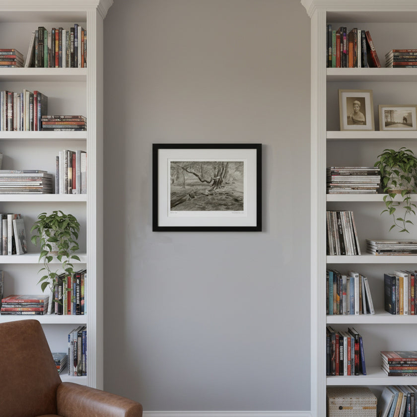 A framed black and white landscape art print hangs on a light grey wall between two tall white bookshelves filled with books and plants.