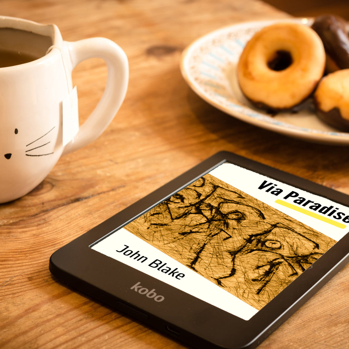 A Kobo e-reader displaying the book cover of 'Via Paradise' abook by John Blake, placed on a wooden table next to a white ceramic mug and a plate of pastries.