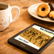 A Kobo e-reader displaying the book cover of 'Via Paradise' abook by John Blake, placed on a wooden table next to a white ceramic mug and a plate of pastries.