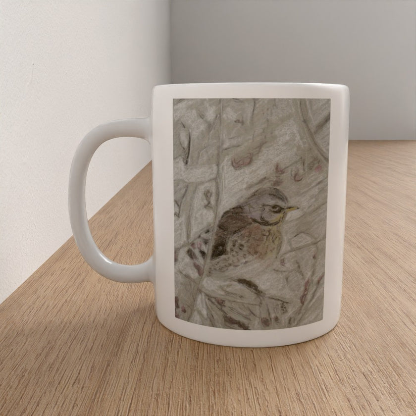 A white ceramic mug with a printed illustration of a small brown bird on a textured gray background, sitting on a light wood tabletop against a neutral wall.