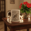 A white ceramic mug featuring a detailed sketch of a bird, placed on a dark wooden table next to a potted plant with red flowers and warm string lights.