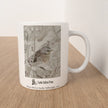 A white ceramic mug with a printed winter bird illustration and the text 'Castle Sefton Press' and 'Winter Bird by Emily Tellwright, 2022', sitting on a light wood surface against a white wall.