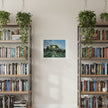 a painting of sun coming through winter trees on a cream wall between two bookcases topped with plants