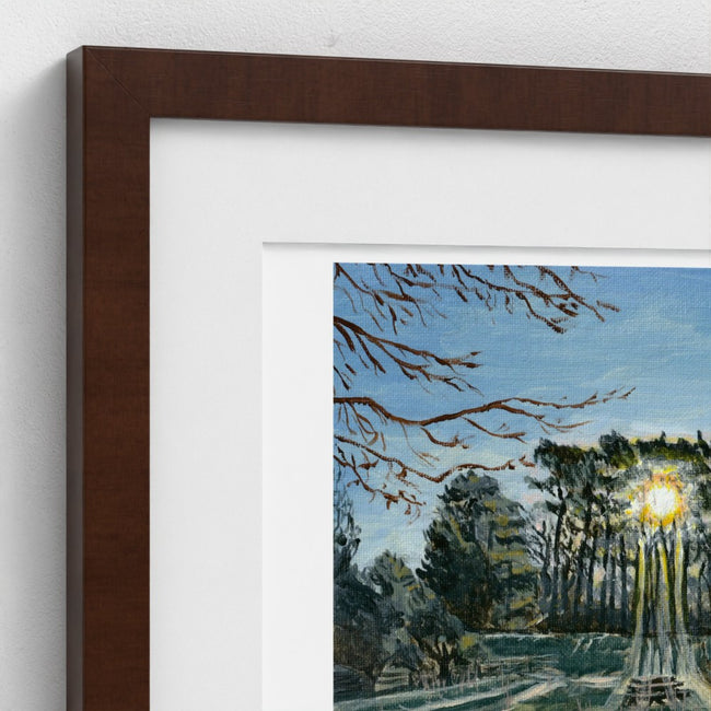 A close-up of a framed art print showing a painted forest scene with green and yellow foliage, a white mat, and a dark brown wooden frame against a white wall.