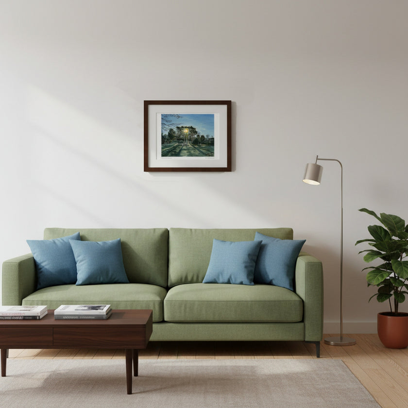 A framed art print depicting a forest path hangs on a mustard yellow wall above a brown leather sofa with green and blue throw pillows. A wooden coffee table with books and a mug sits in the foreground.