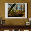 An art print depicting a woodland scene with bare trees and a path, mounted on a patterned gold wallpaper wall above a dark wooden mantel with other framed pictures.
