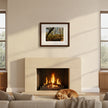 A framed forest landscape art print hangs above a fireplace in a modern living room setting with a dog sleeping on the rug below.