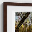 A framed art print featuring an impressionistic painting of a forest with a prominent leaning tree, styled with a dark brown frame and white matting against a light gray wall.