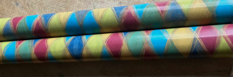 Two rolls of patterned wrapping paper with a colorful harlequin diamond design in blue, magenta, yellow, and teal, displayed on a neutral surface.