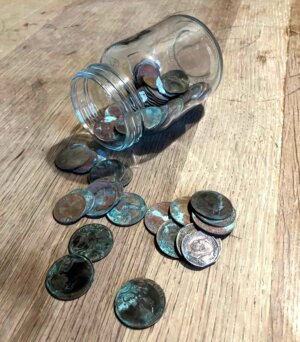 Donations for readers of second hand copies: Glass jar on its side on a table with old coins spilling out.