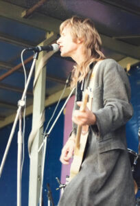 John Blake on stage playing guitar and singing into a microphone