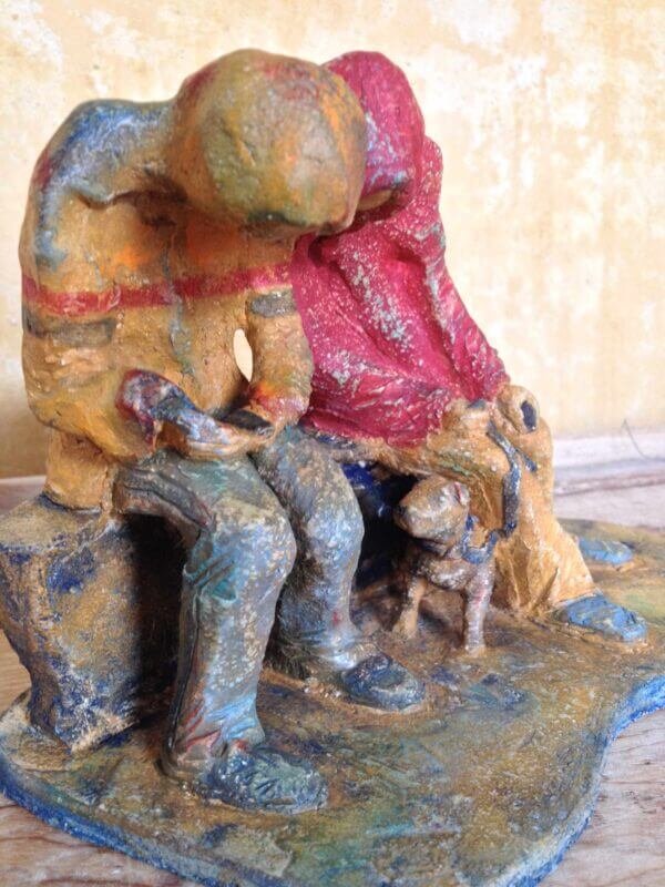 Ceramic sculpture of two figures sitting in hoodies looking at mobile phones with a dog at their feet.