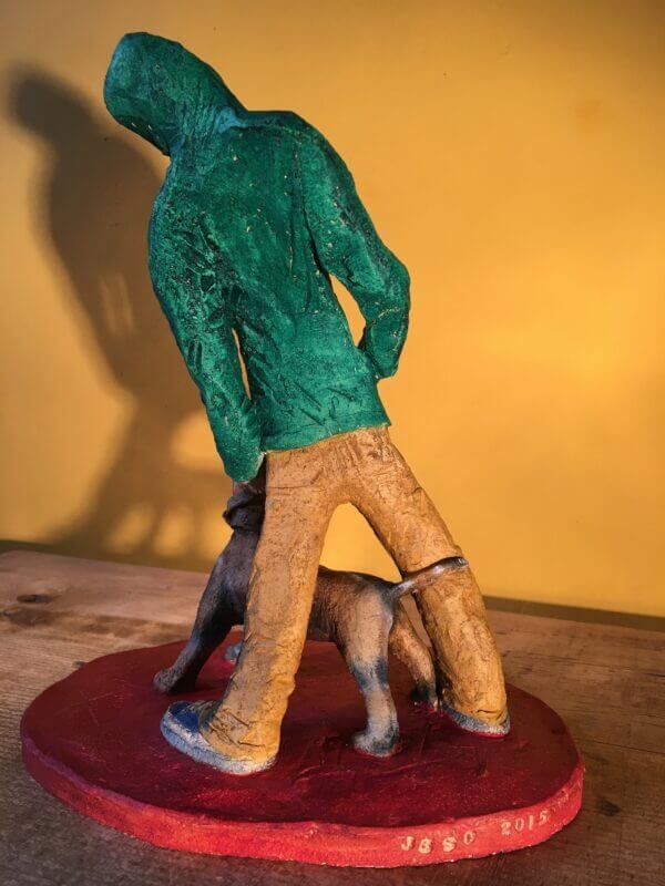 Ceramic sculpture of figure in green hoodie with a Staffordshire bull terrier on a lead.