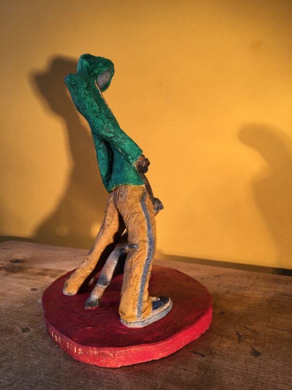 Ceramic sculpture of figure in green hoodie with a Staffordshire bull terrier on a lead.