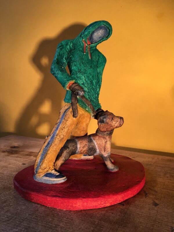 Ceramic sculpture of figure in green hoodie with a Staffordshire bull terrier on a lead.
