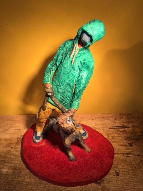 Ceramic sculpture of figure in green hoodie with a Staffordshire bull terrier on a lead.