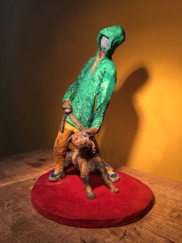 Ceramic sculpture of figure in green hoodie with a Staffordshire bull terrier on a lead.