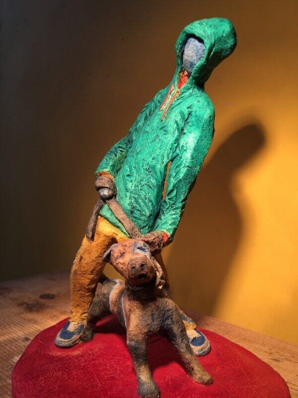 Ceramic sculpture of figure in green hoodie with a Staffordshire bull terrier on a lead.