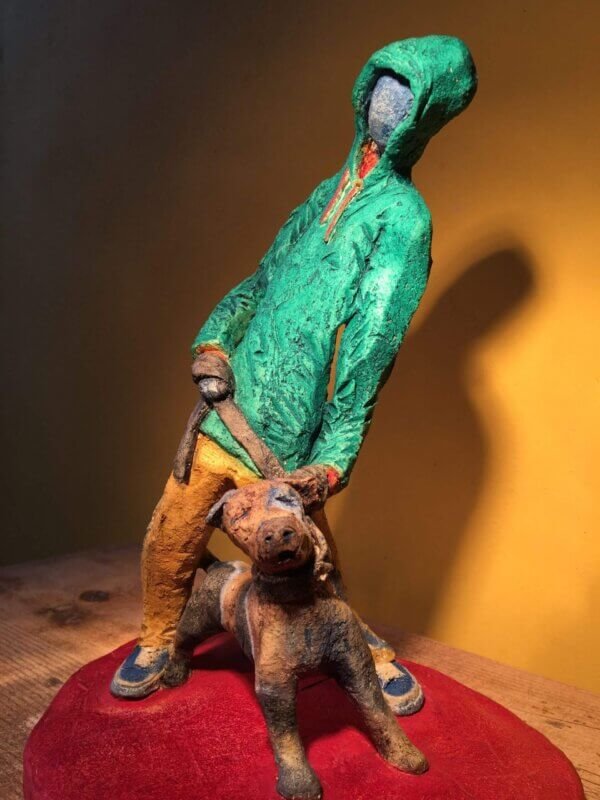 Ceramic sculpture of figure in green hoodie with a Staffordshire bull terrier on a lead.