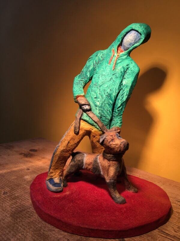 Ceramic sculpture of figure in green hoodie with a Staffordshire bull terrier on a lead.