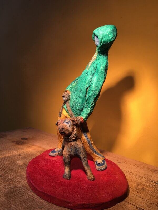 Ceramic sculpture of figure in green hoodie with a Staffordshire bull terrier on a lead.