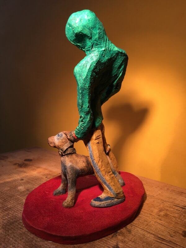 Ceramic sculpture of figure in green hoodie with a Staffordshire bull terrier on a lead.