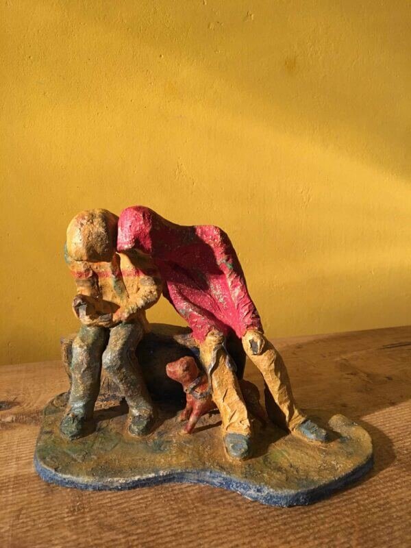 Ceramic sculpture of two figures sitting in hoodies looking at mobile phones with a dog at their feet.