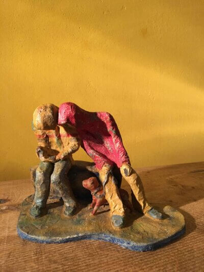 Ceramic sculpture of two figures sitting in hoodies looking at mobile phones with a dog at their feet.