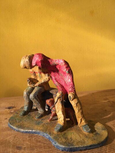Ceramic sculpture of two figures sitting in hoodies looking at mobile phones with a dog at their feet.