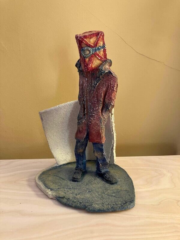 ceramic sculpture of a figure with a box and goggles on its head