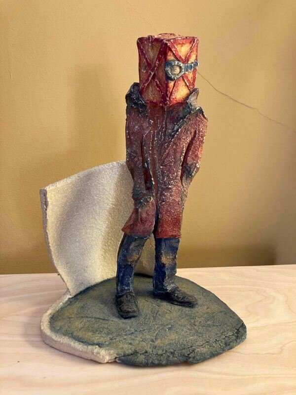 ceramic sculpture of a figure with a box and goggles on its head