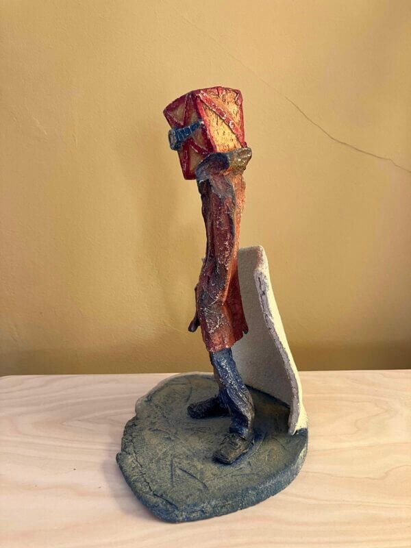ceramic sculpture of a figure with a box and goggles on its head