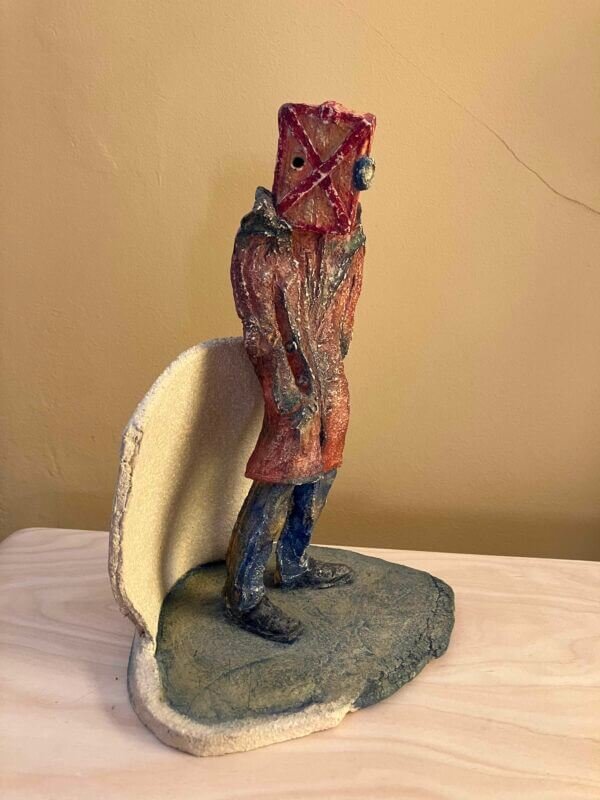 ceramic sculpture of a figure with a box and goggles on its head