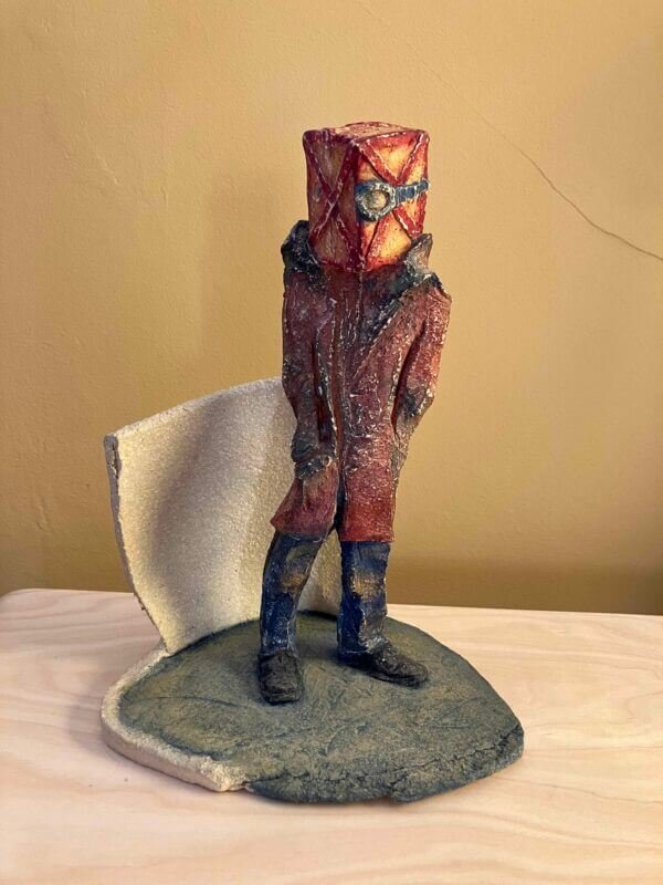 ceramic sculpture of a figure with a box and goggles on its head