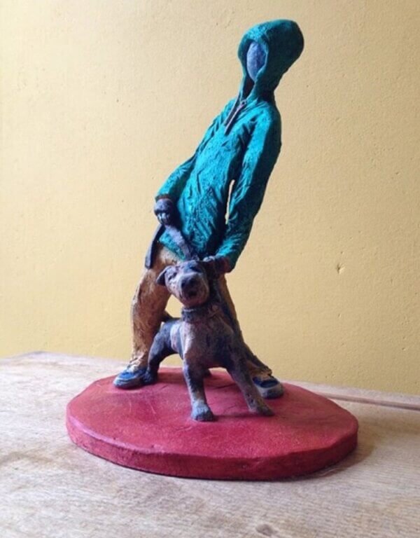 Ceramic sculpture of figure in green hoodie with a Staffordshire bull terrier on a lead.