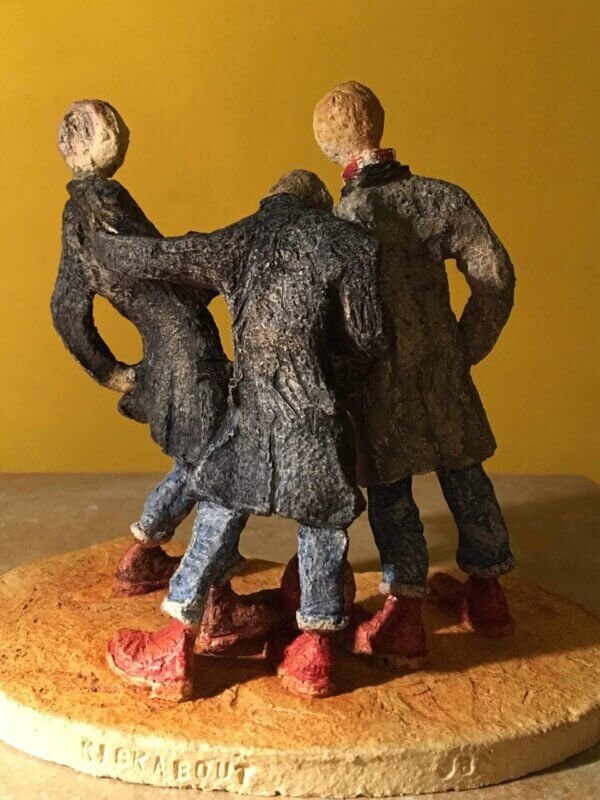 ceramic sculpture of figures in coats kicking a football around