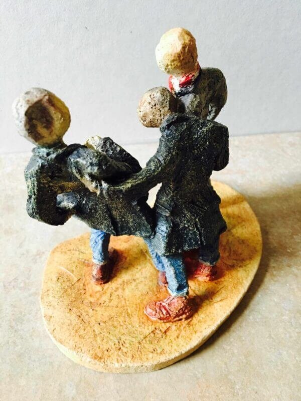 ceramic sculpture of figures in coats kicking a football around