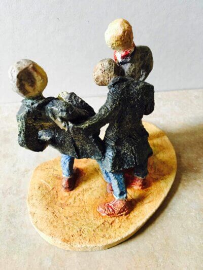 ceramic sculpture of figures in coats kicking a football around