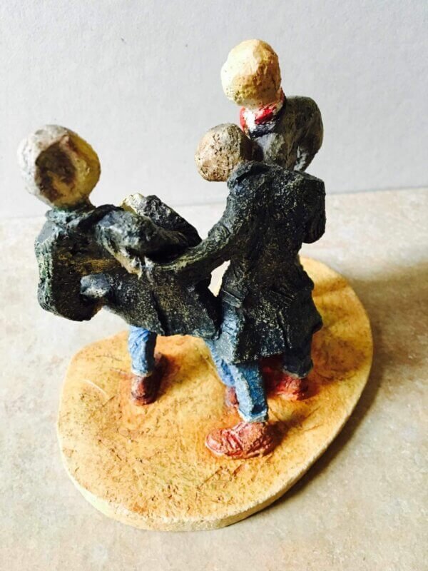 ceramic sculpture of figures in coats kicking a football around