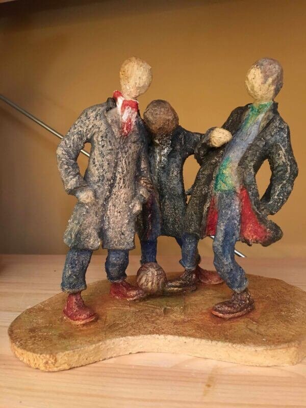 ceramic sculpture of figures in coats kicking a football around