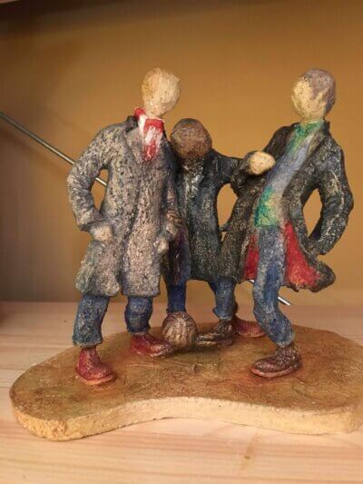 ceramic sculpture of figures in coats kicking a football around