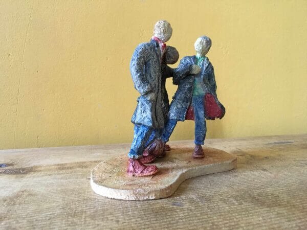 ceramic sculpture of figures in coats kicking a football around