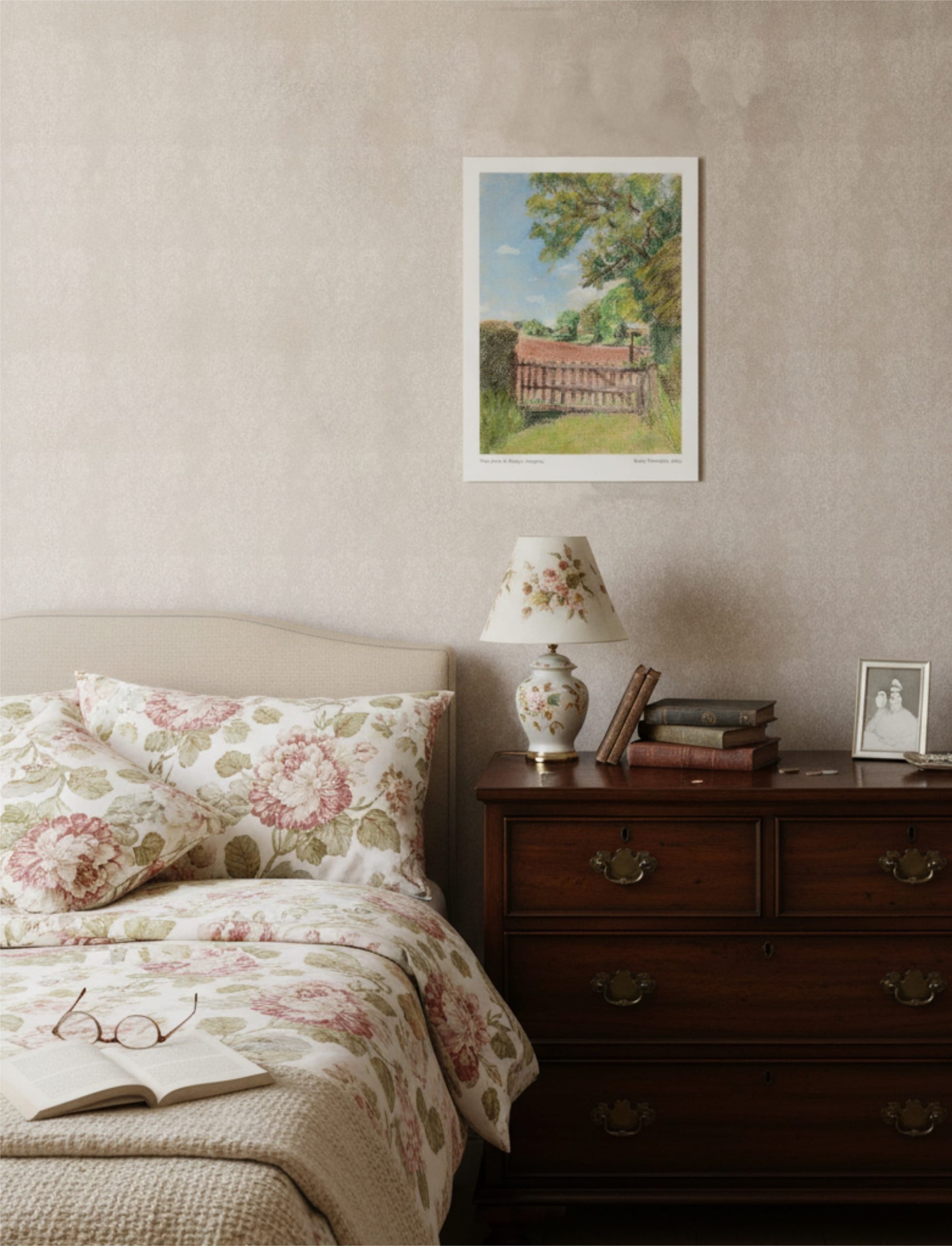 The view from St Mary's Kempley Art Print on the wall above a bed with chintz cover and a chest of drawers with a lamp on