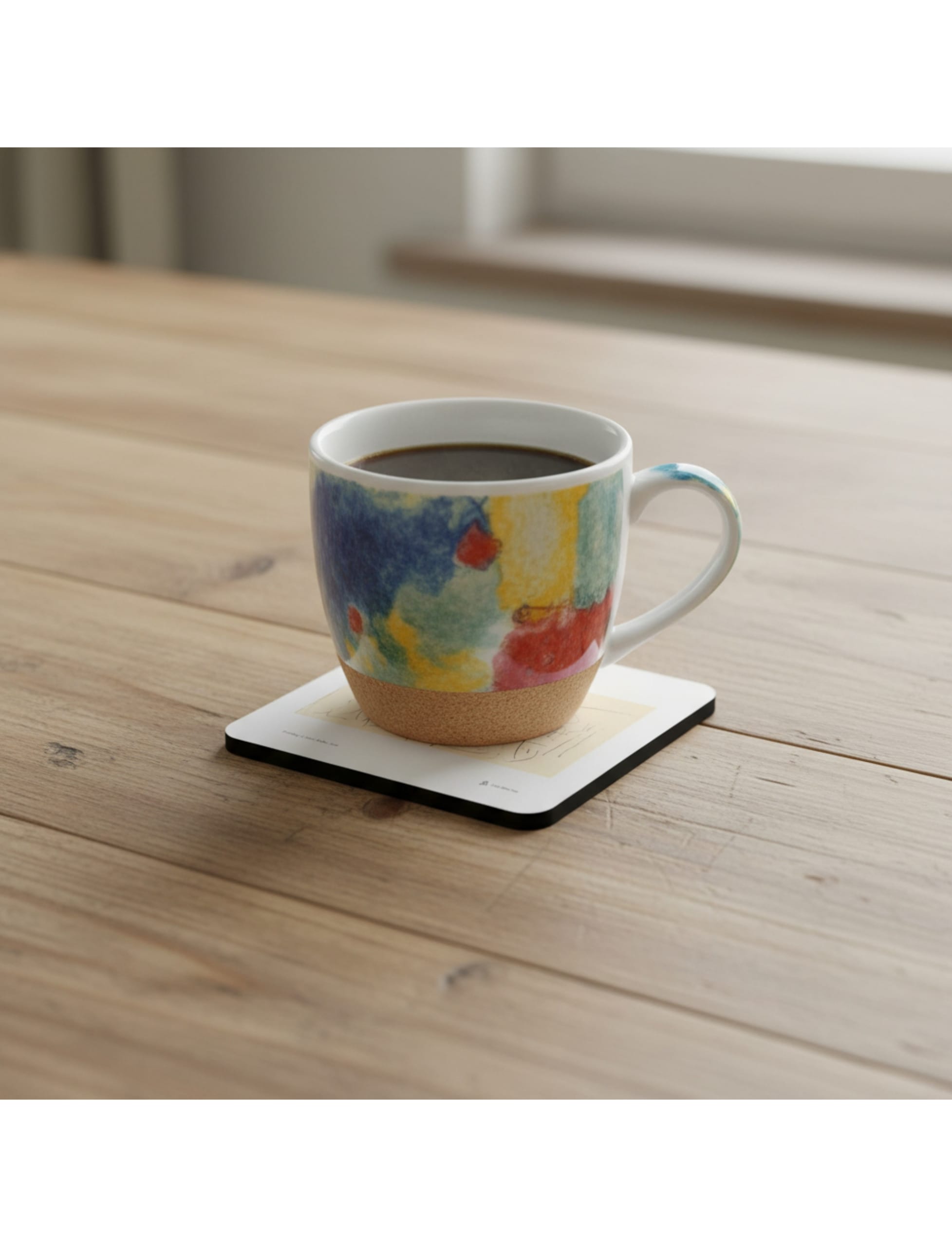 Frühling Coaster showing a pencil drawing by John Blake on a table with a coffee cup on it